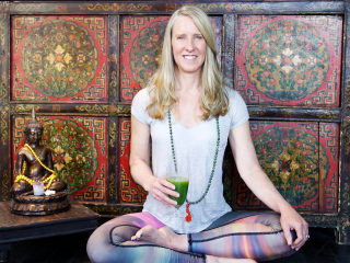 Tanya Mark sitting in the lotus position while holding a smoothie next to a Buddha statue.
