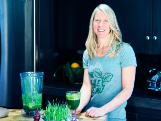 Tanya Mark standing next to a table with vegetables and a smoothie in a blender and a glass.