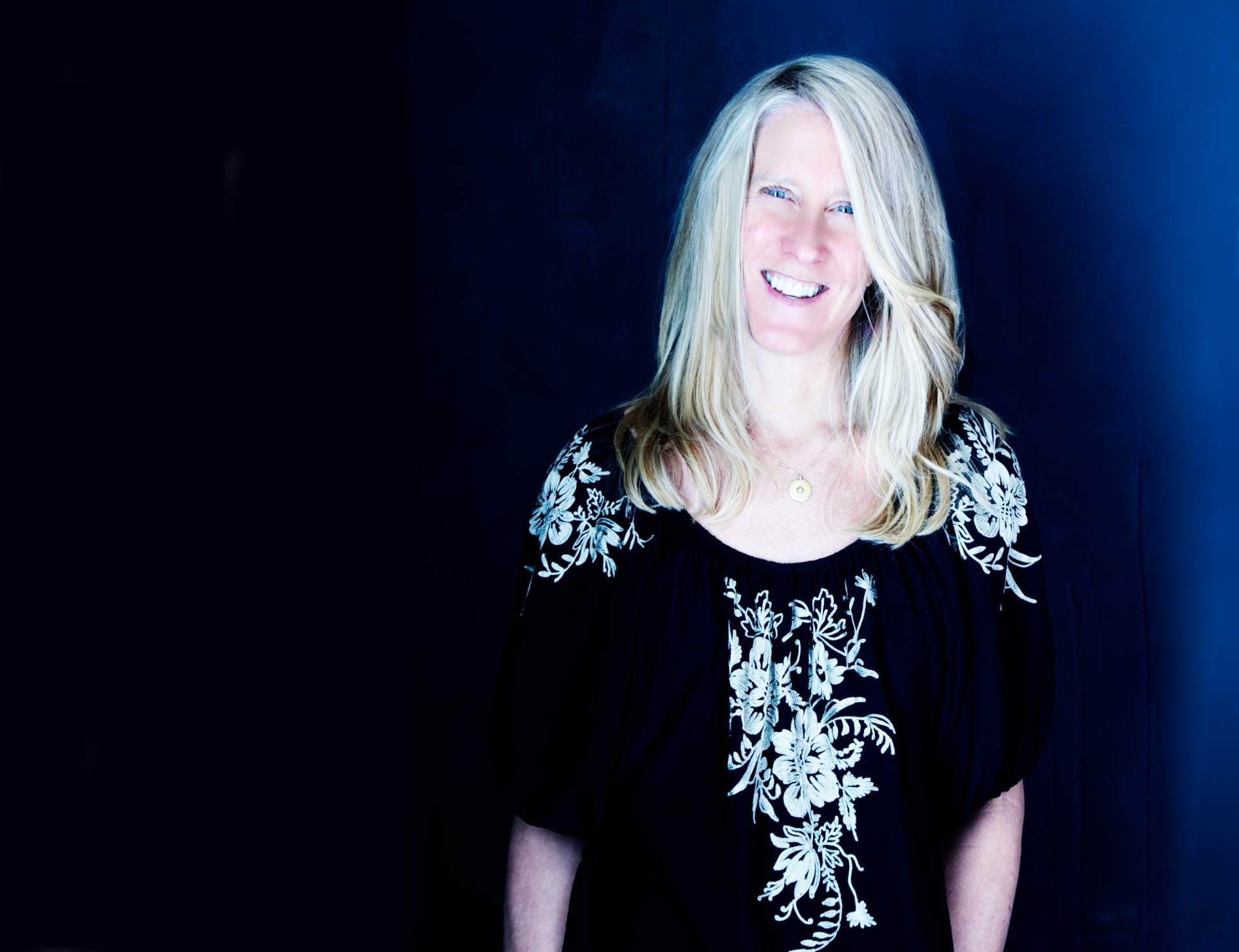 Online nutrition coach Tanya Mark smiles while standing in front of a blue background.